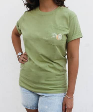 Camiseta verde da marca Corona com um limão estampado no bolso, localizado na parte superior esquerda da camiseta.