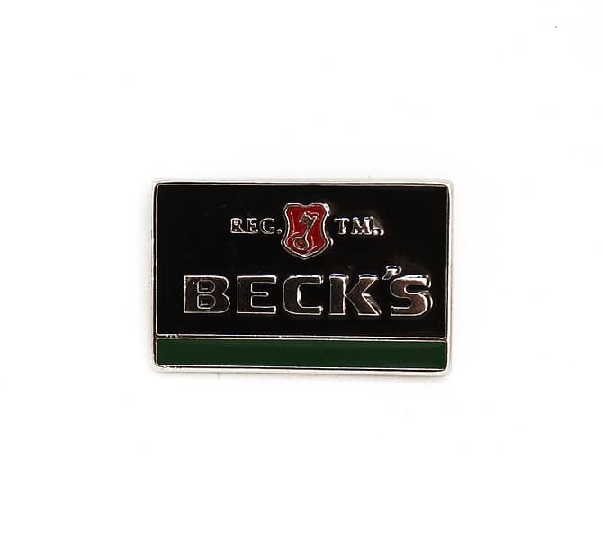 Pin em metal nas cores preto e verde com logo em alto relevo escrito "Becks Reg TM