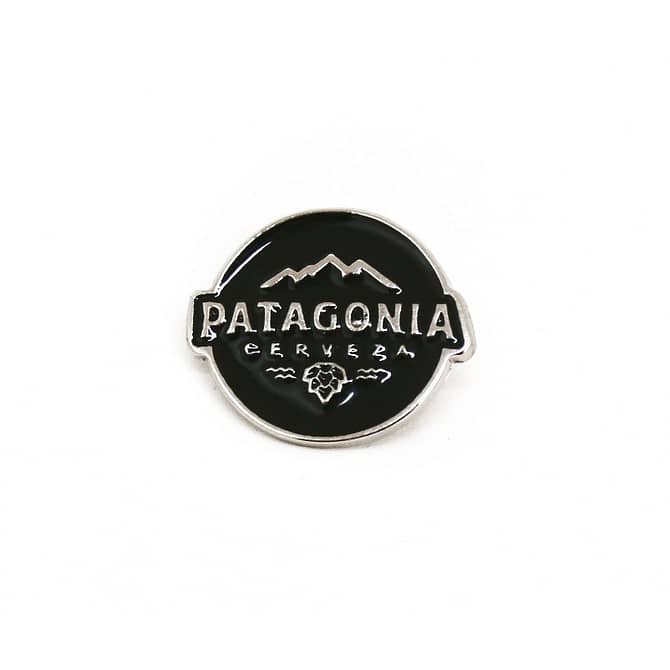 Pin metálico circular verde com estampa em alto relevo que representa uma montanha na parte superior, o texto "Patagonia Cervejaria" no centro e um lúpulo na parte inferior